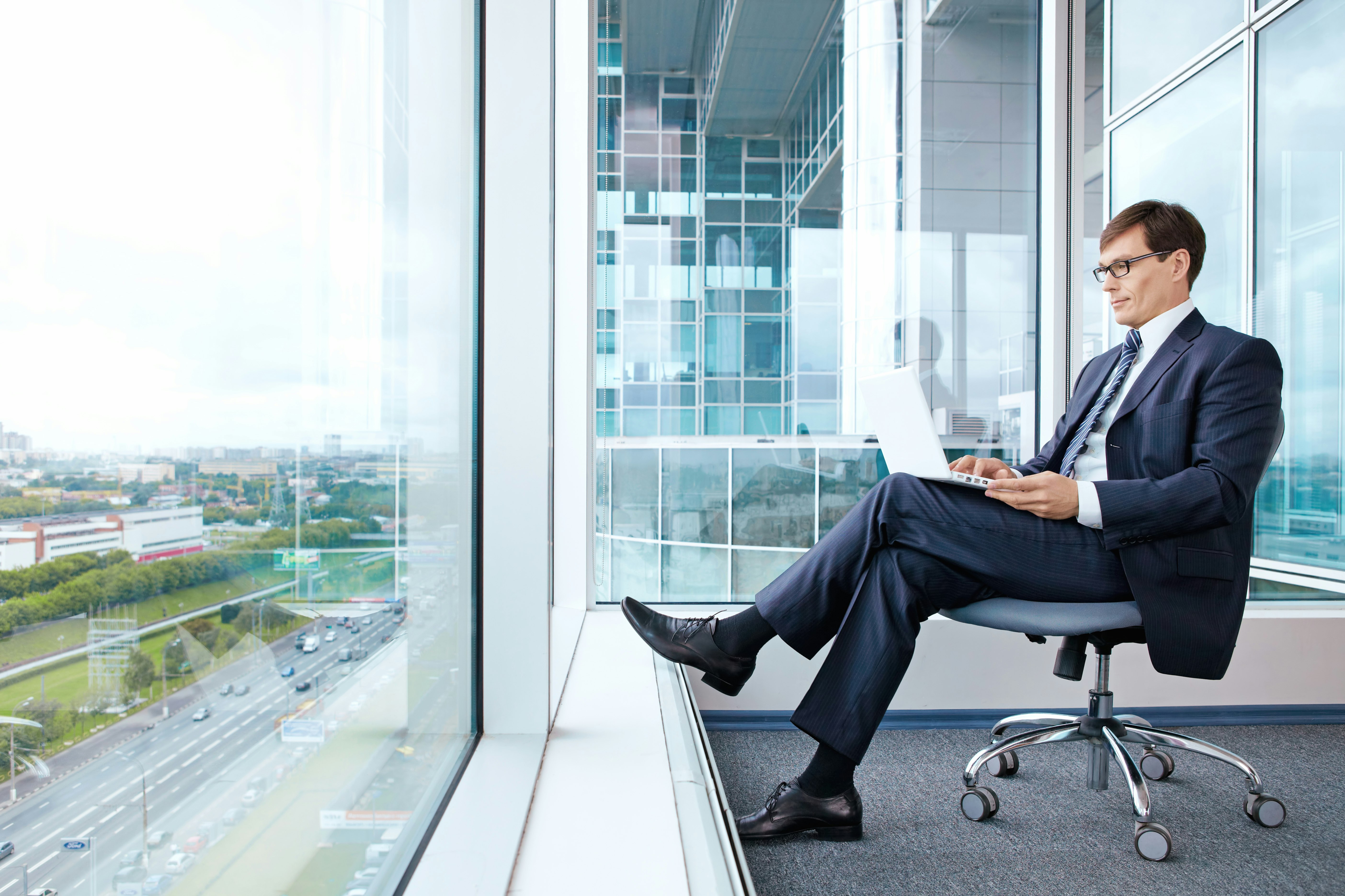 The man works for a laptop in the office with a view from the window