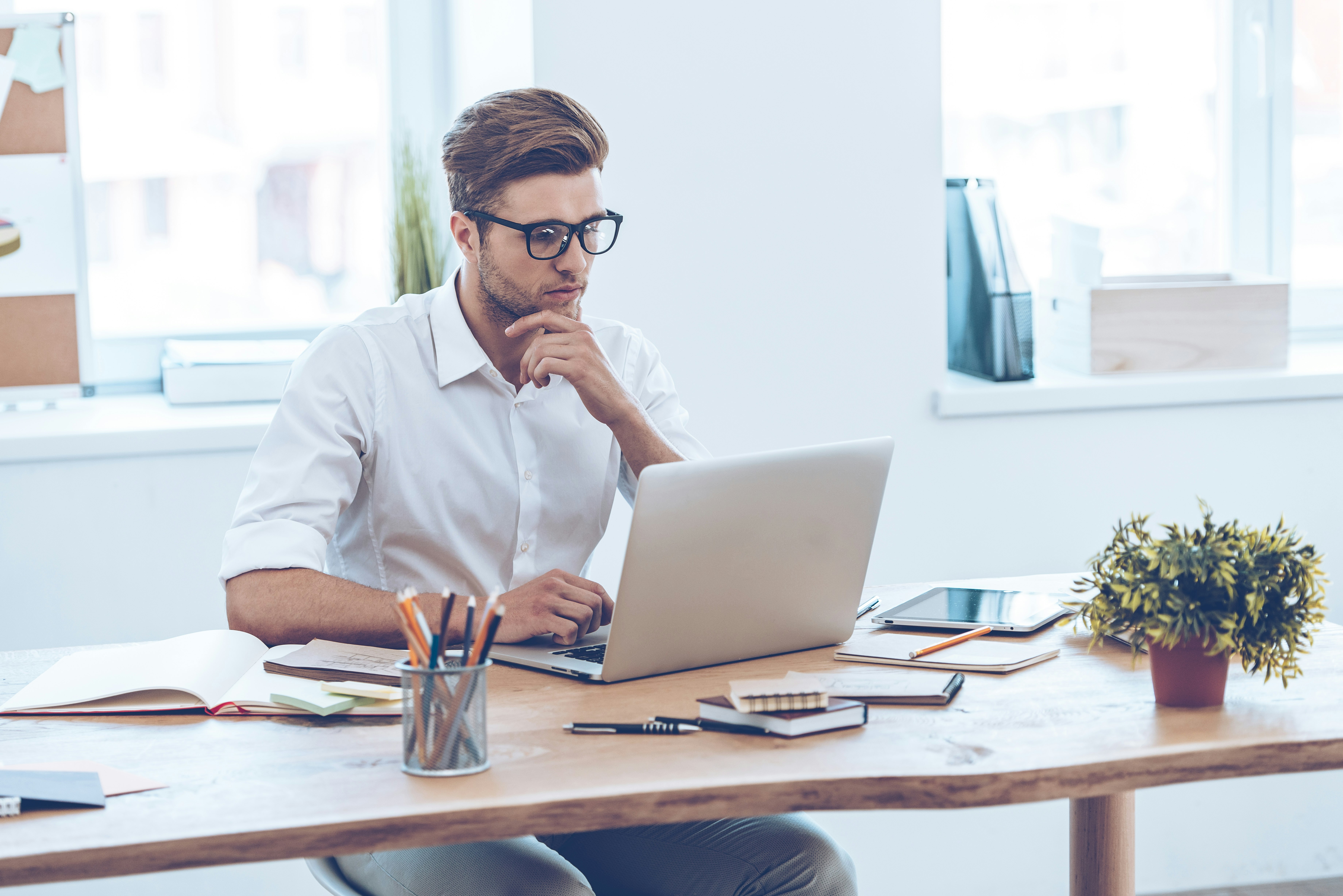 Confident expert at work. Pensive young handsome man using his laptop while sitting at his working place